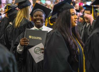 graduates wearing caps and gowns hold diplomas and programs