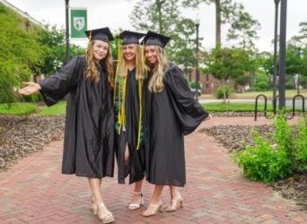 three graduates in black gowns and caps posing outdoors at abraham baldwin agricultural college