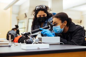 students in lab coats using a microscope