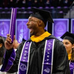 graduate excitedly holding diploma at commencement