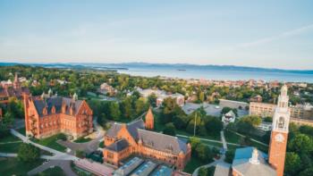 An aerial view of the UVM campus, surrounded by green trees and a scenic lakeside